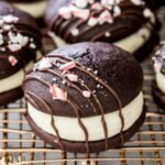 peppermint bark whoopie pies drizzled with chocolate and topped with crushed candy canes on gold metal cooling rack