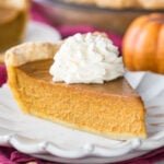 slice of homemade pumpkin pie topped with whipped cream on white plate