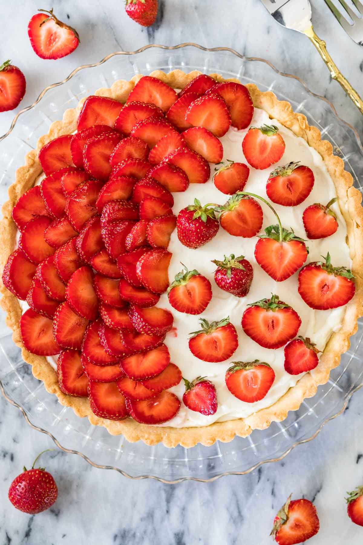 Overhead view of a strawberry tart with half of the tart covered in strawberry slices and the other half with strawberry halves.