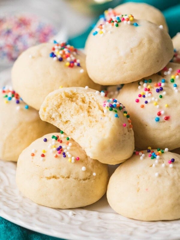 Pile of Italian cookies on a plate with one cookie missing a bite.
