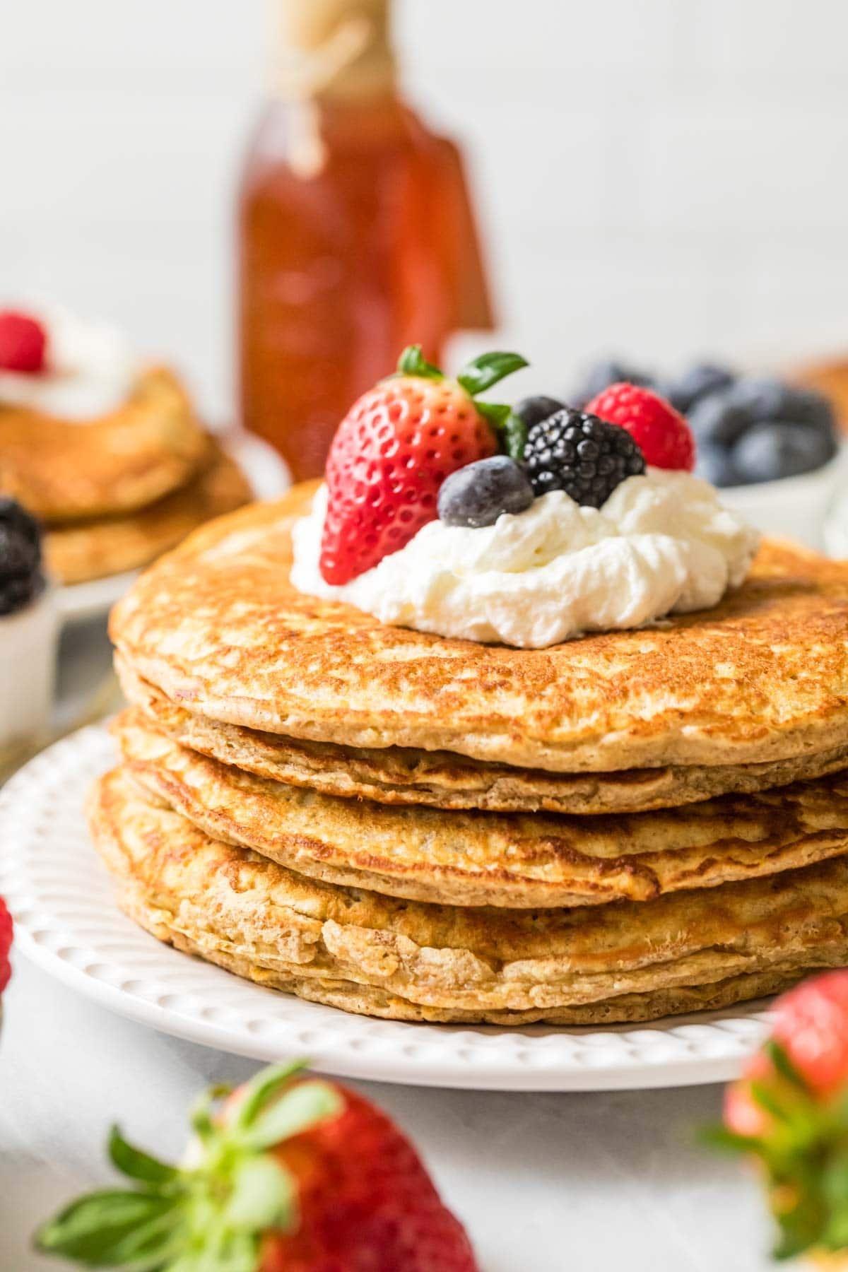 Stack of whole wheat pancakes topped with whipped cream and berries.