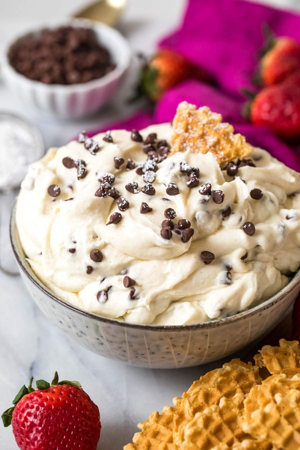 Bowl of cannoli dip topped with mini chocolate chips and a pizzelle cookie.