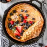 Overhead view of a Dutch baby topped with fresh berries and powdered sugar in a cast iron skillet.