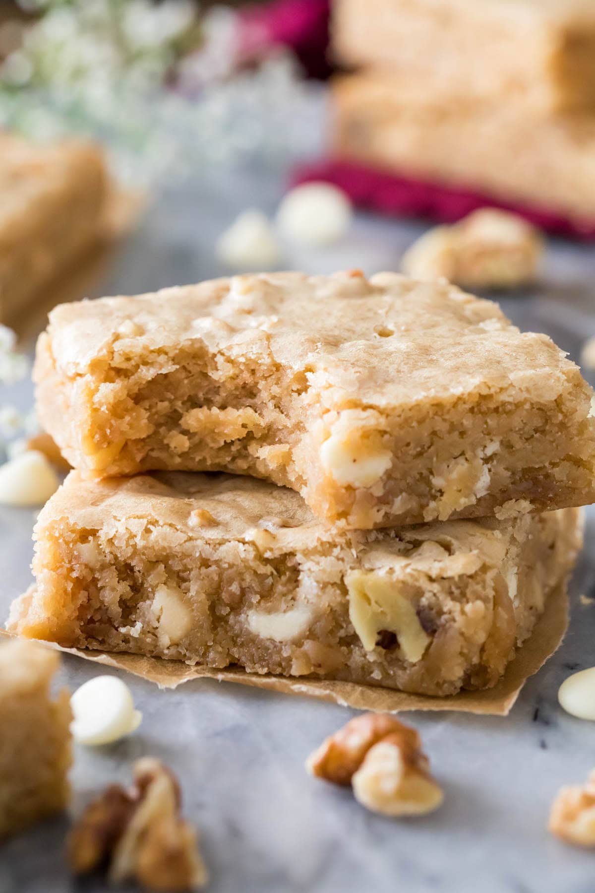 2 slices of my iconic blondie recipe, stacked on one another with a bite missing from the top piece. bits of white chocolate and walnut visible.