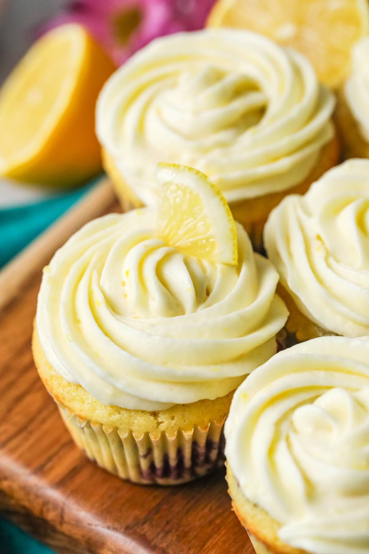 Close-up view of cupcakes topped with swirls of lemon cream cheese frosting and a tiny lemon wedge.