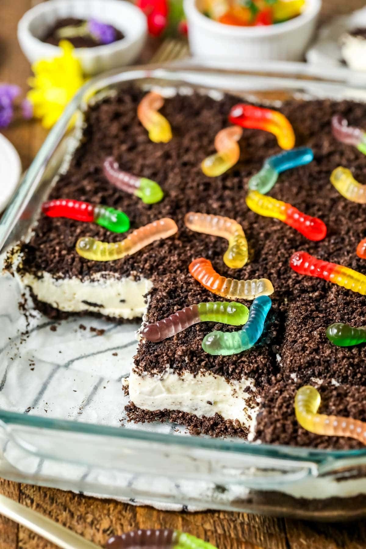 Slices missing from a pan of homemade dirt cake made with Oreo cookie crumbs, a cream cheese filling, and gummy worms.