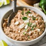 Bowl of homemade refried beans topped with cheese and cilantro.