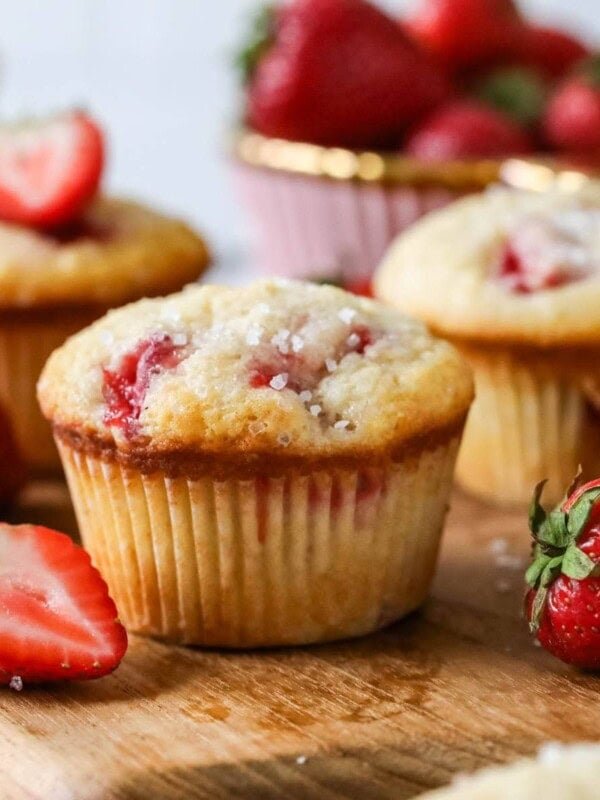 Strawberry muffins with sparkling sugar tops on a wood serving board.