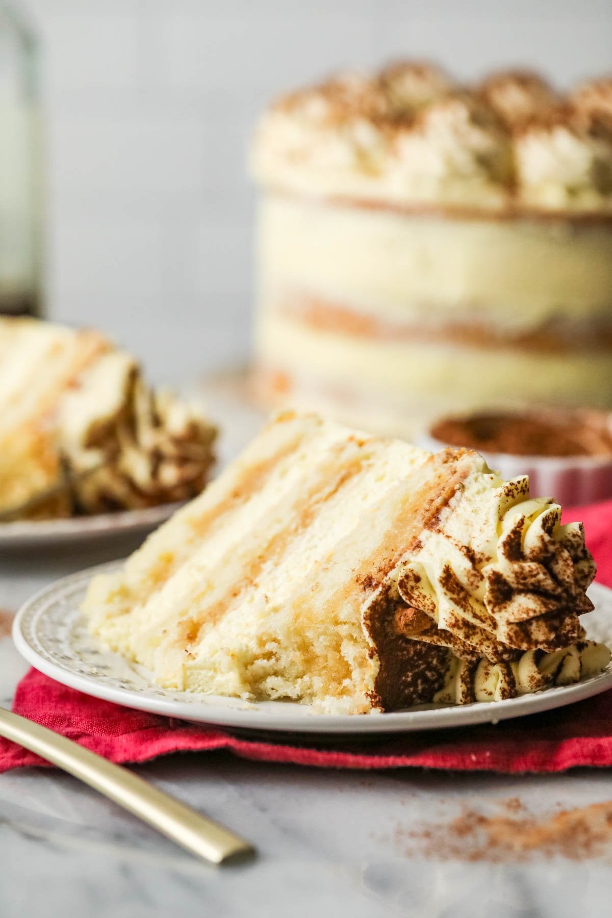 Slice of tiramisu layer cake with one bite missing on a plate.