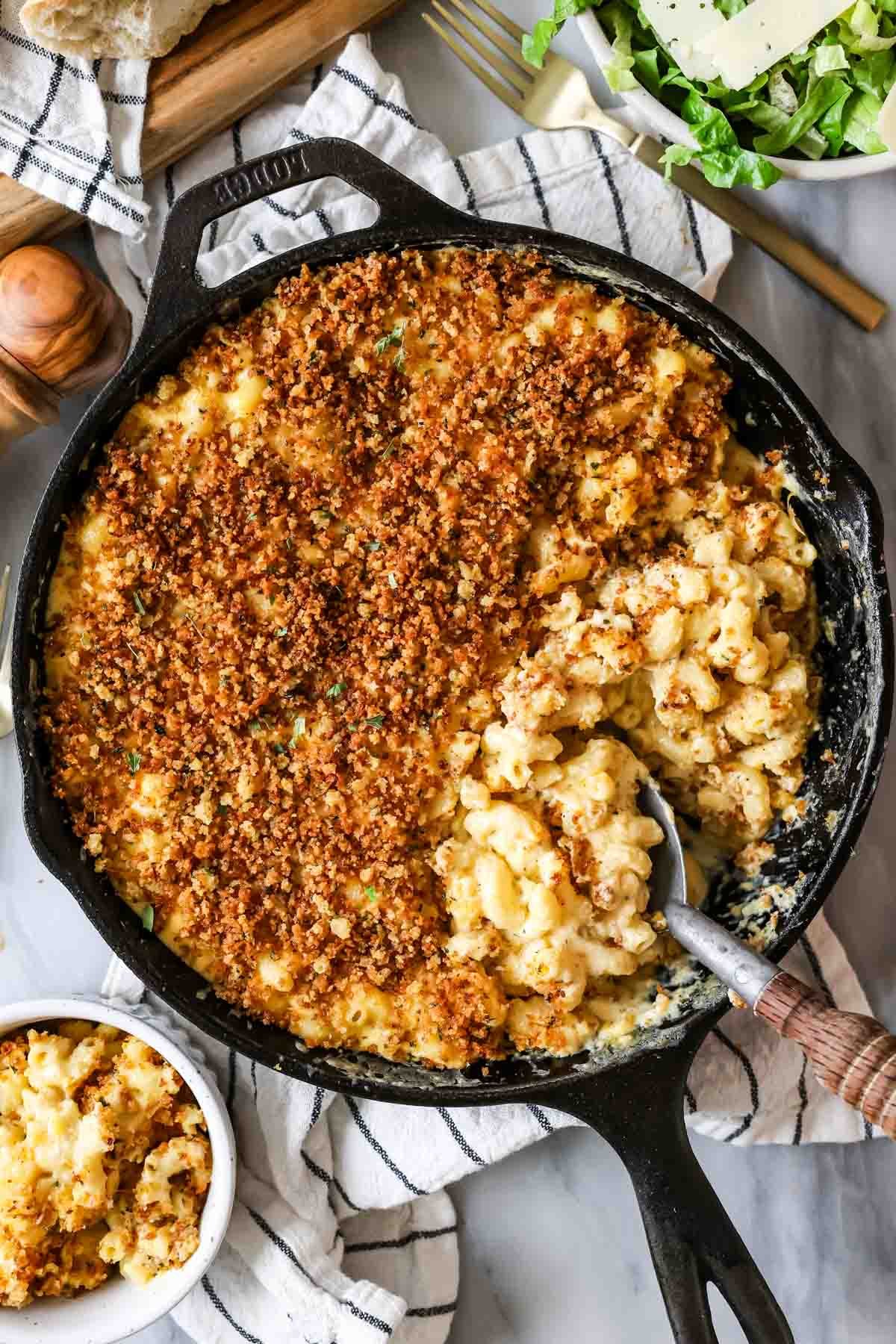 The creamiest, easiest, BEST Baked Mac and Cheese Recipe! This is so good! #macandcheese #dinnerrecipe #kidfriendlyrecipe Overhead view of baked mac and cheese in a cast iron skillet -- serving spoon showing cheesy macaroni beneath crisp panko topping.