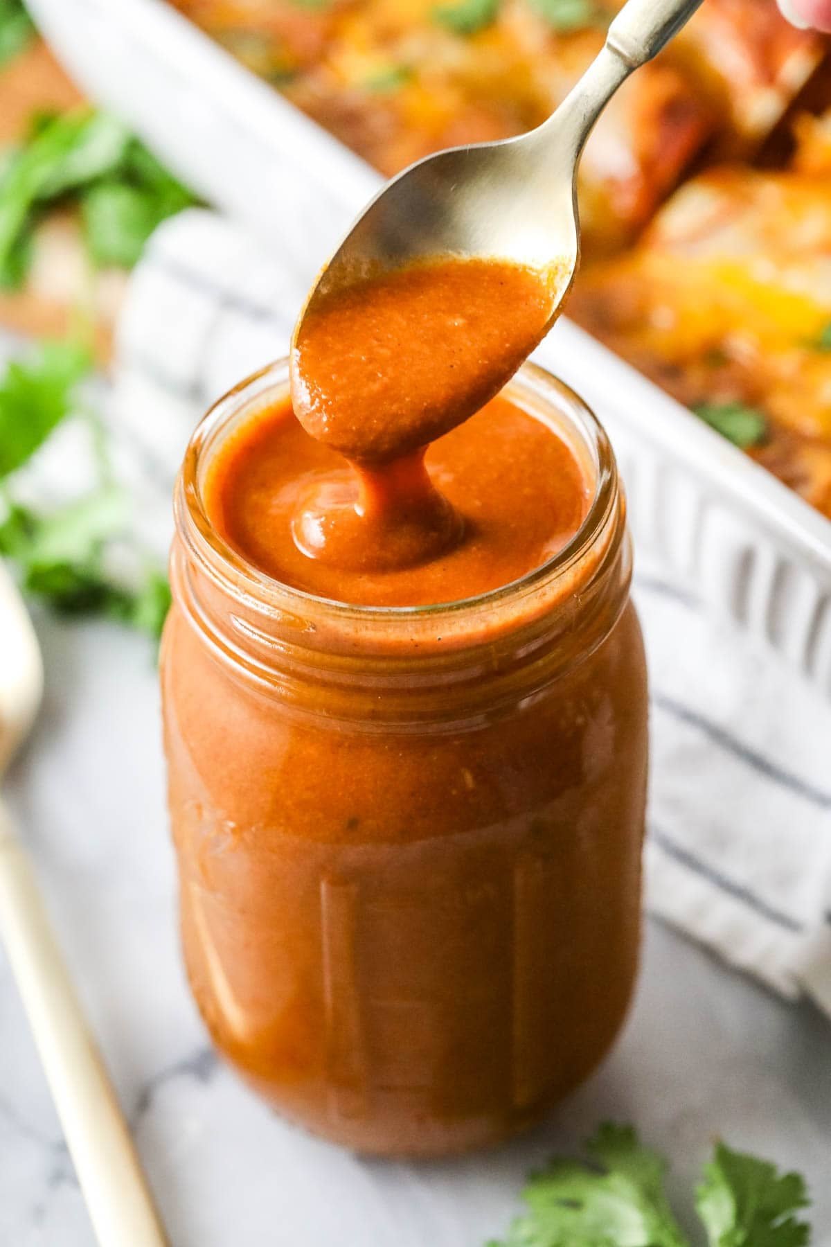 Homemade enchilada sauce being spooned from a jar.