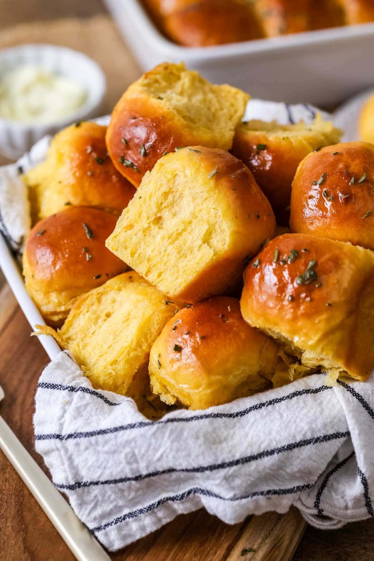 Pile of golden brown sweet potato dinner rolls topped with a garlic rosemary butter.
