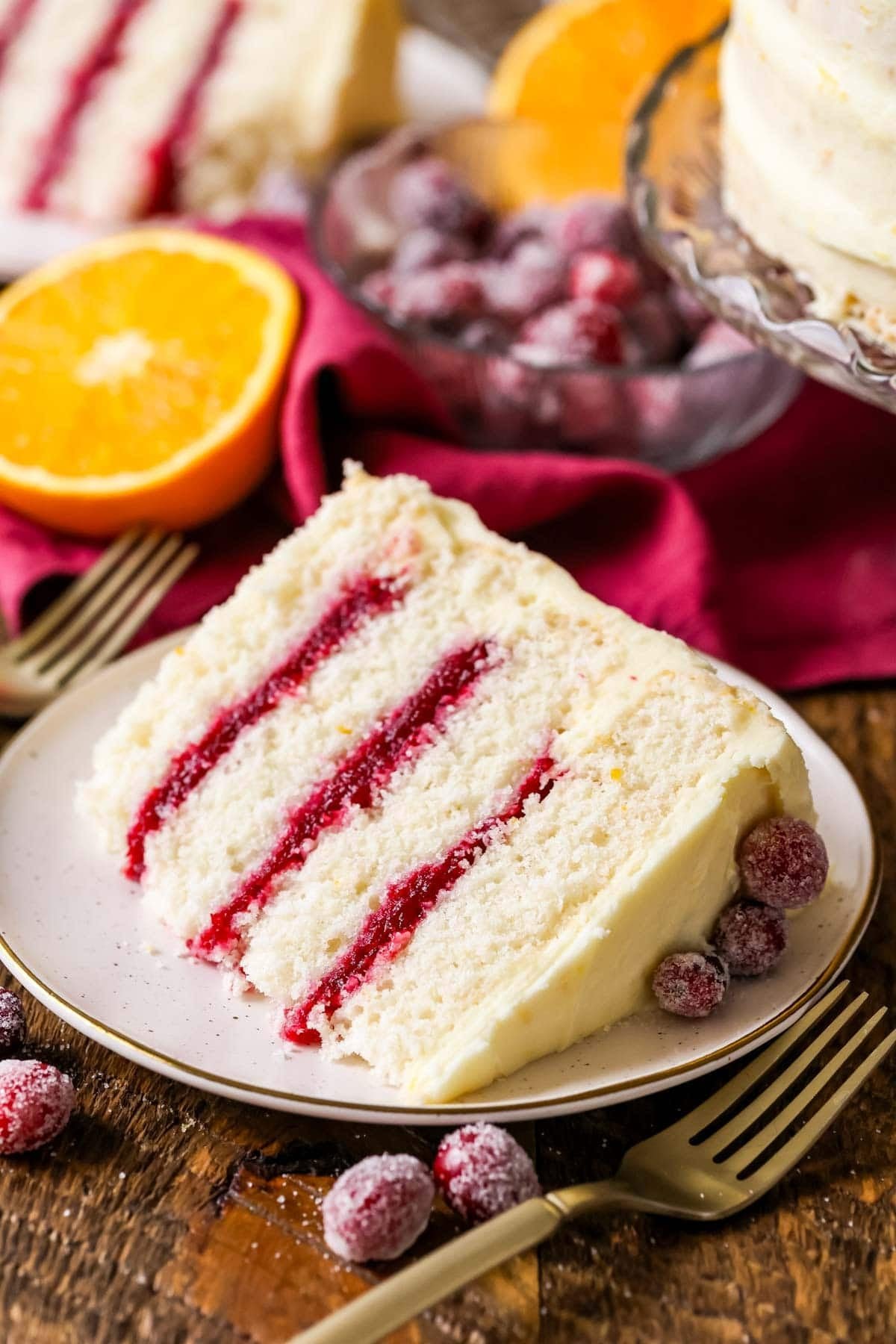Slice of cranberry orange cake made with a cranberry sauce filling and orange cream cheese frosting on a plate.