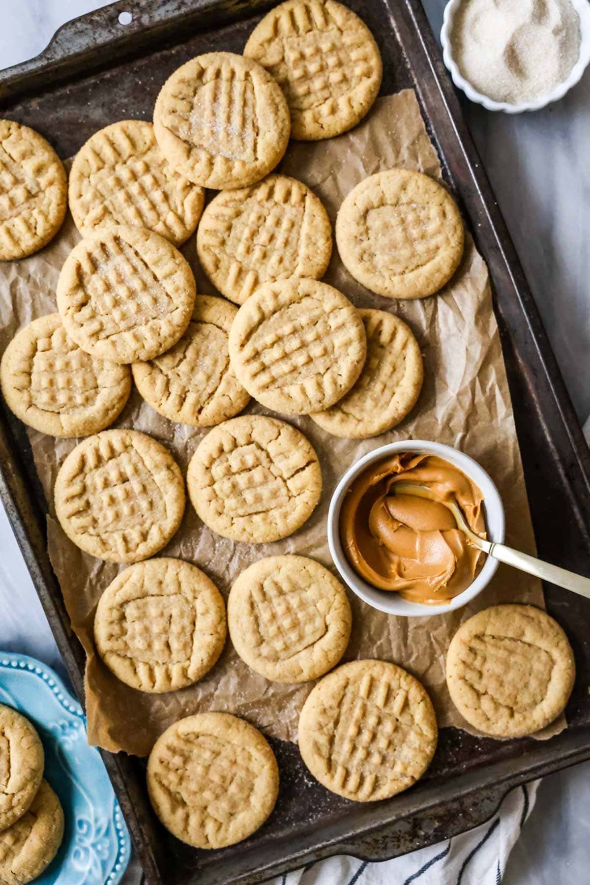 Overhead view of peanut butter cookies next to a bowl of peanut butter on a parchment lined baking sheet.